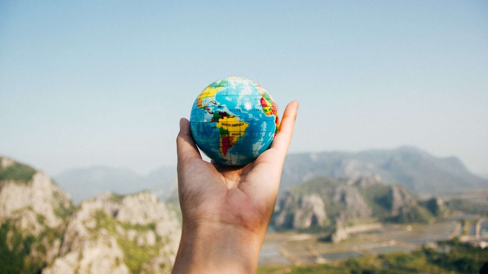 person holding world globe facing mountain