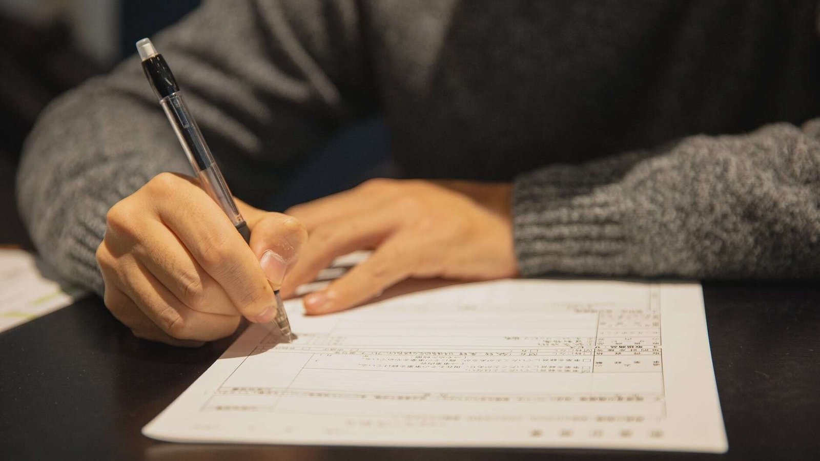 man filling in form on parer at table