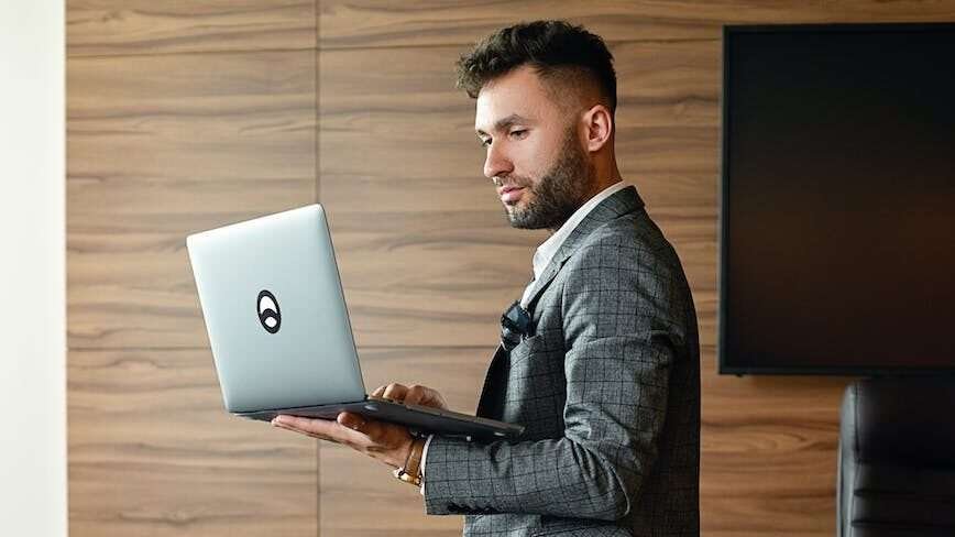 office worker leaning on a table while holding a laptop