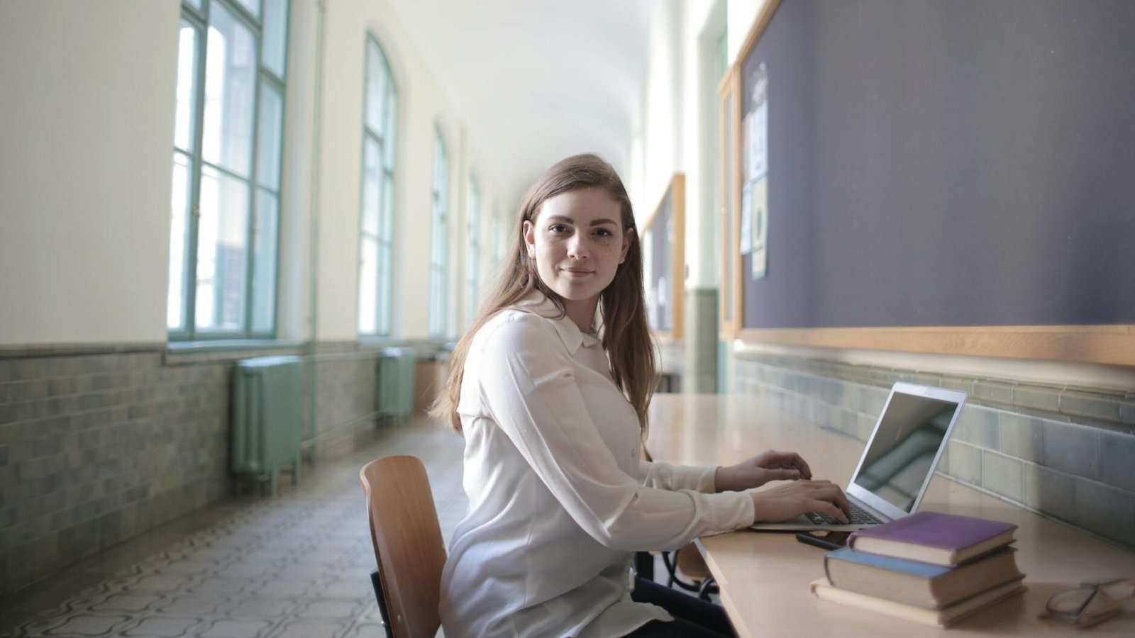 female student typing on laptop in university hallway