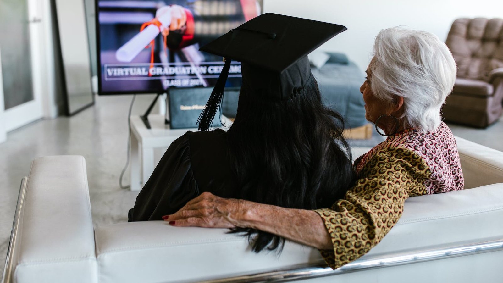 back view shot of a grandmother sitting beside her granddaughter wearing black graduation cap