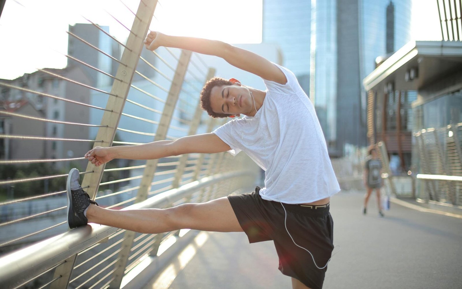 young slender ethnic sportsman in earbuds warming up and listening to music with pleasure on street in city